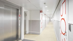 Un pasillo moderno con suelo de madera clara, paredes blancas y círculos rojos en las puertas.