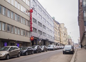 Fila de coches aparcados a lo largo de una calle con edificios que muestran letreros de un hotel y una cafetería.