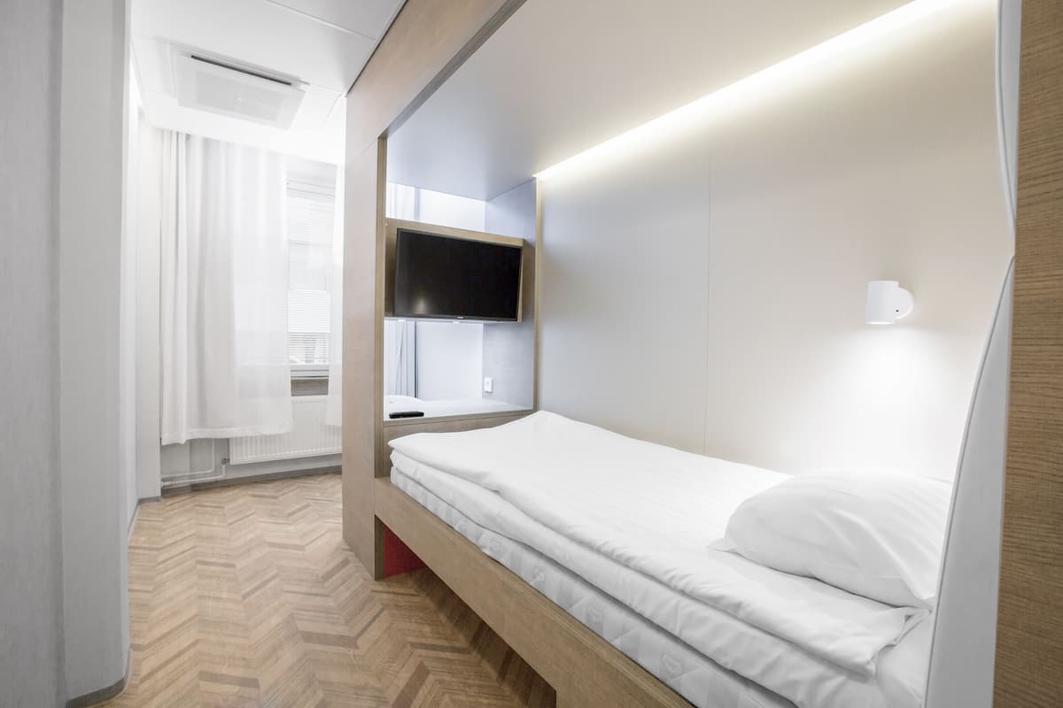 Une chambre d’hôtel moderne avec un cadre de lit en bois, un téléviseur fixé au mur et une lampe de chevet.