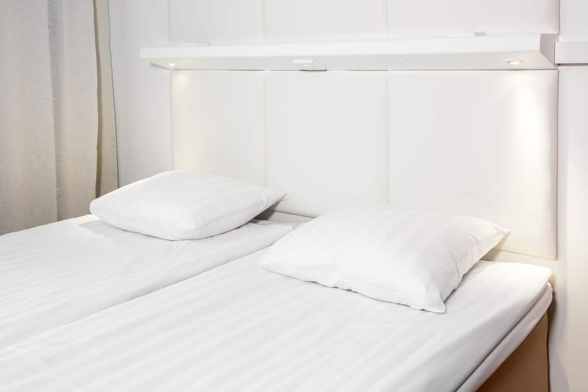 Un lit avec du linge de lit blanc et des oreillers, une tête de lit dotée d’un éclairage intégré et un mur sobre.