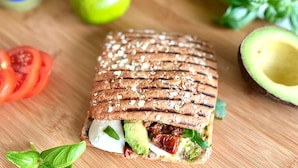 Un sándwich de aguacate, tomate y queso sobre una tabla de madera.