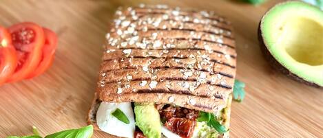 A sandwich with avocado, tomato, and cheese on a wooden cutting board.