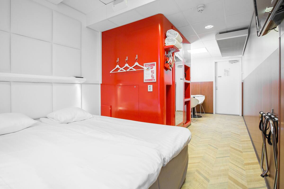Une chambre d’hôtel avec un lit, une armoire rouge, un petit coin salon et un plancher en bois.