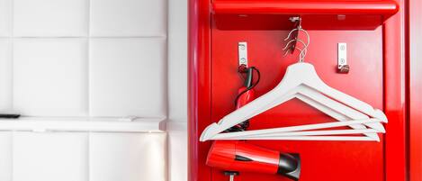 Une armoire rouge avec une tringle pour suspendre les vêtements et un sèche-cheveux à l’intérieur.