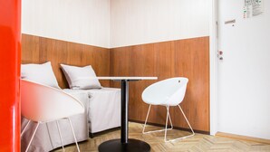 Habitación de esquina con un revestimiento de madera, una mesa redonda, dos sillas blancas y una cama con ropa de cama blanca.