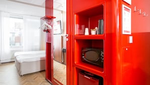 Habitación con marco rojo, una cama, un microondas y un pequeño estante con objetos.
