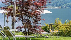 A lakeside terrace with lounge chairs, umbrellas, and a table with drinks. - Dependence del Parco (Porlezza)
