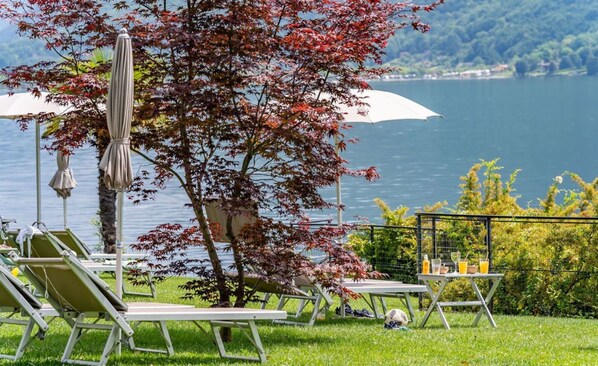 A lakeside terrace with lounge chairs, umbrellas, and a table with drinks.