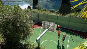 An outdoor basketball court with a net, surrounded by greenery and a lake view. - Dependence del Parco (Porlezza)