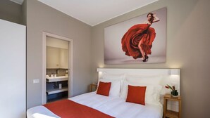 A hotel room with a large bed, a nightstand with a lamp, a painting on the wall, and a bathroom visible through an open door. - Dependence del Parco (Porlezza)