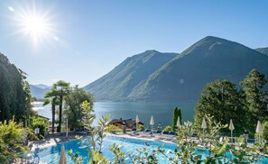 Un área de piscina con sillas de descanso y sombrillas, rodeada de montañas y un lago.