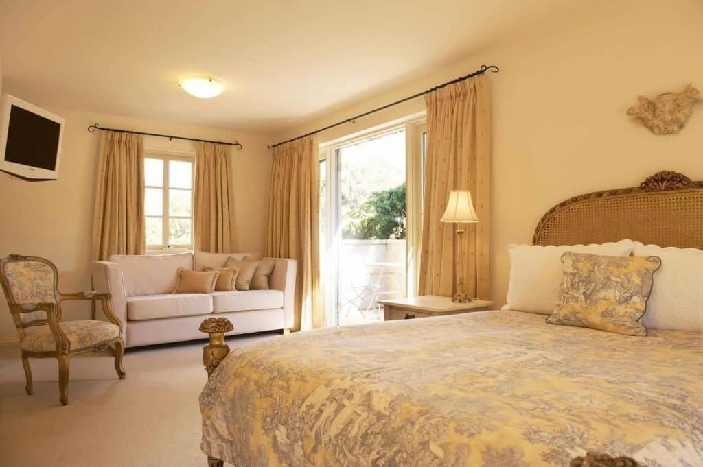 A hotel room with a bed, a sofa, a chair, a lamp, and a television.