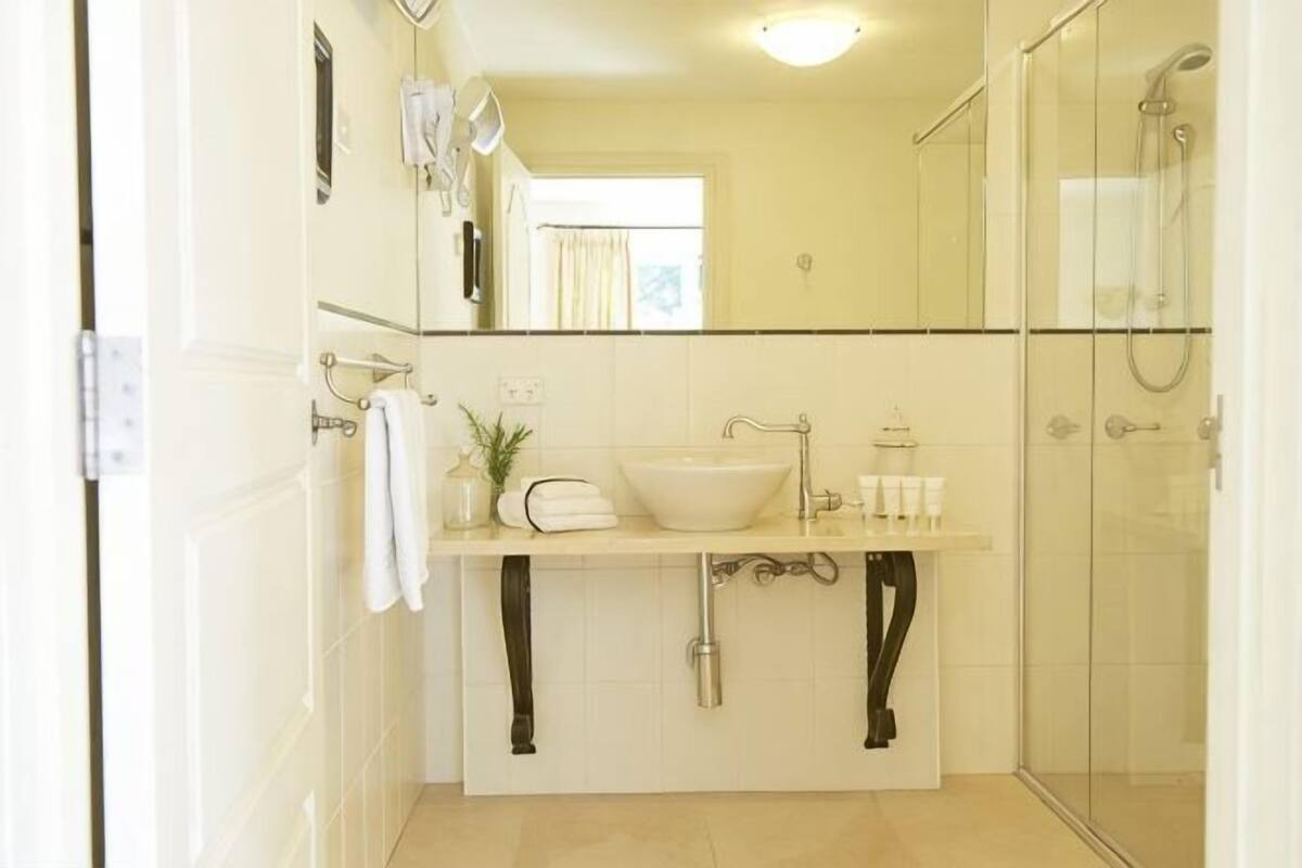 Un baño con lavamanos, espejo, toallero, ducha y cabina de ducha de vidrio.