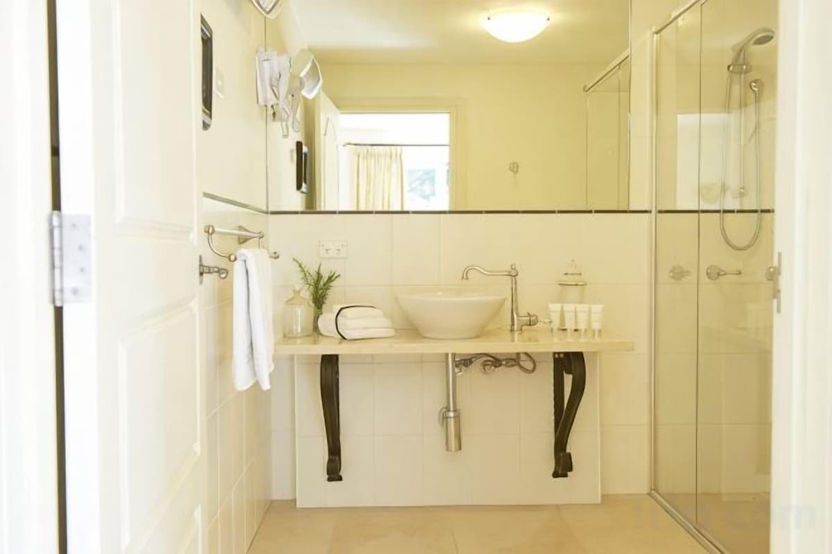 A bathroom with a sink, mirror, towel rack, and shower.
