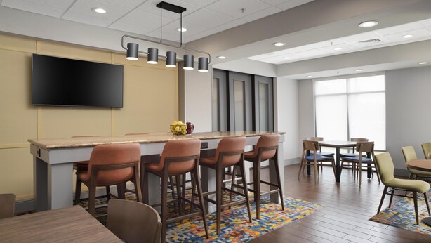 A modern bar area with a flat-screen TV, bar stools, and a patterned rug. - Hampton Inn Magnolia (Magnolia)