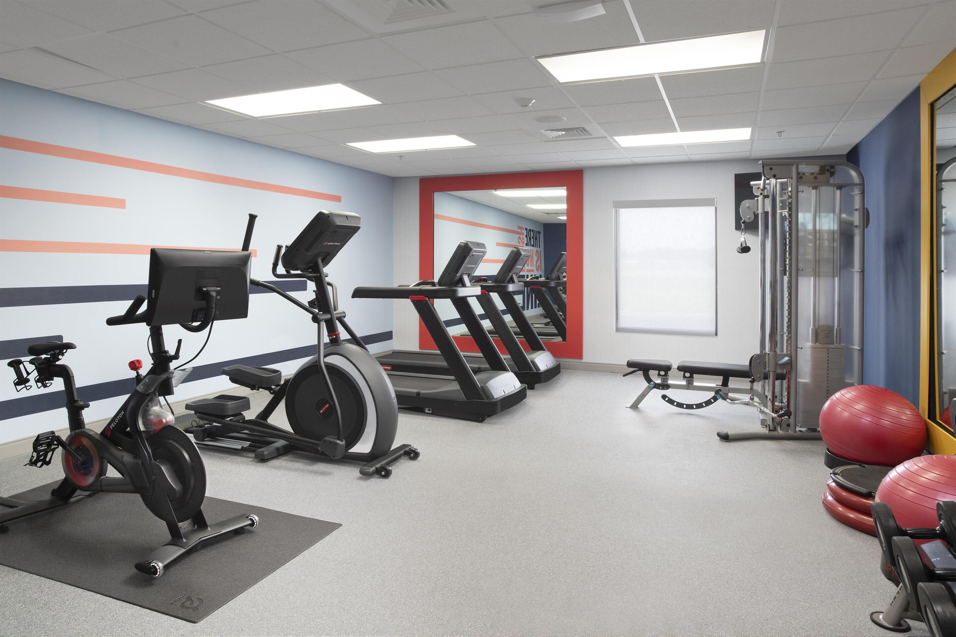 Un gimnasio con equipo de ejercicio, cinta de correr, elíptica y un espejo.