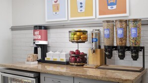 A kitchen area with a coffee machine, a fruit bowl, cereal dispensers, and a refrigerator.