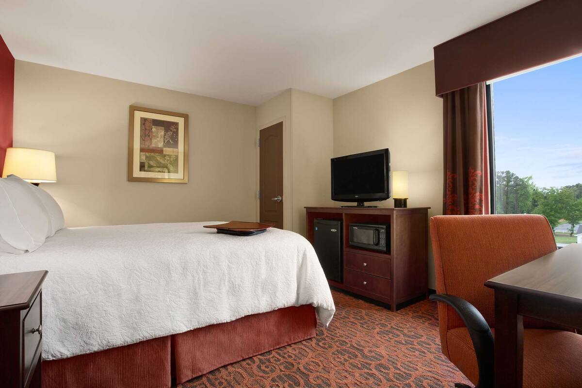 A hotel room with a bed, a television, a desk, and a chair.