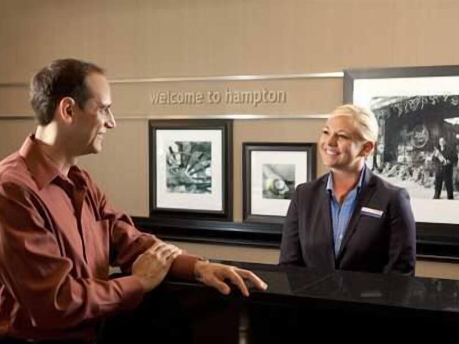 Un mostrador de recepción con un cartel que dice 'Welcome to Hampton', obras de arte enmarcadas en la pared y una fotografía en blanco y negro.