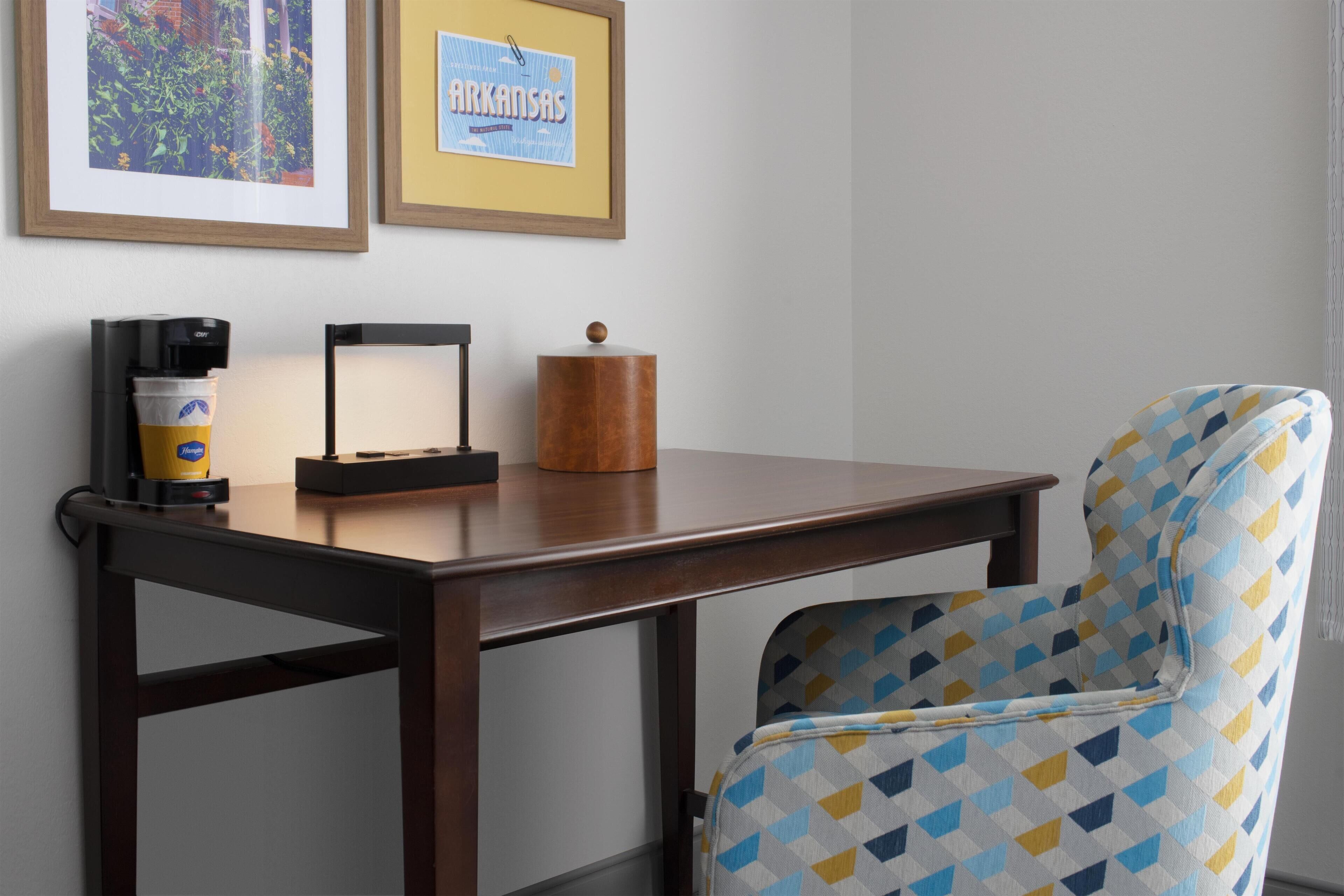 Una habitación con una mesa de madera, una silla estampada, una cafetera y cuadros en la pared.