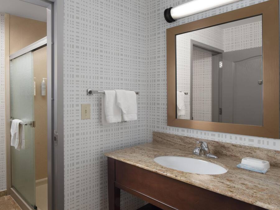 A bathroom with a glass shower door, a sink with a marble countertop, and a mirror with a wooden frame.