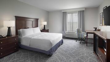 Habitación de hotel con una cama grande, dos mesitas de noche con lámparas, un escritorio con silla y un ventanal con cortinas.