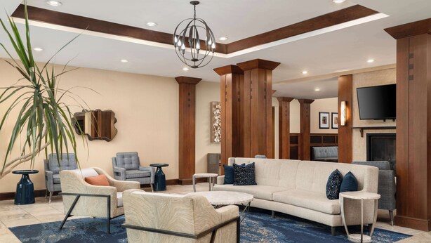 A spacious living area with a large sofa, armchairs, a coffee table, and a TV mounted on the wall. - Homewood Suites by Hilton Newport Middletown, RI (Middletown)