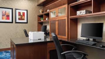 A modern office space with a wooden desk, two chairs, a computer, and framed artwork on the wall.