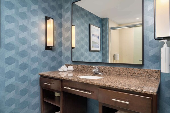 A bathroom with a granite countertop, a sink, a mirror, and a towel rack.