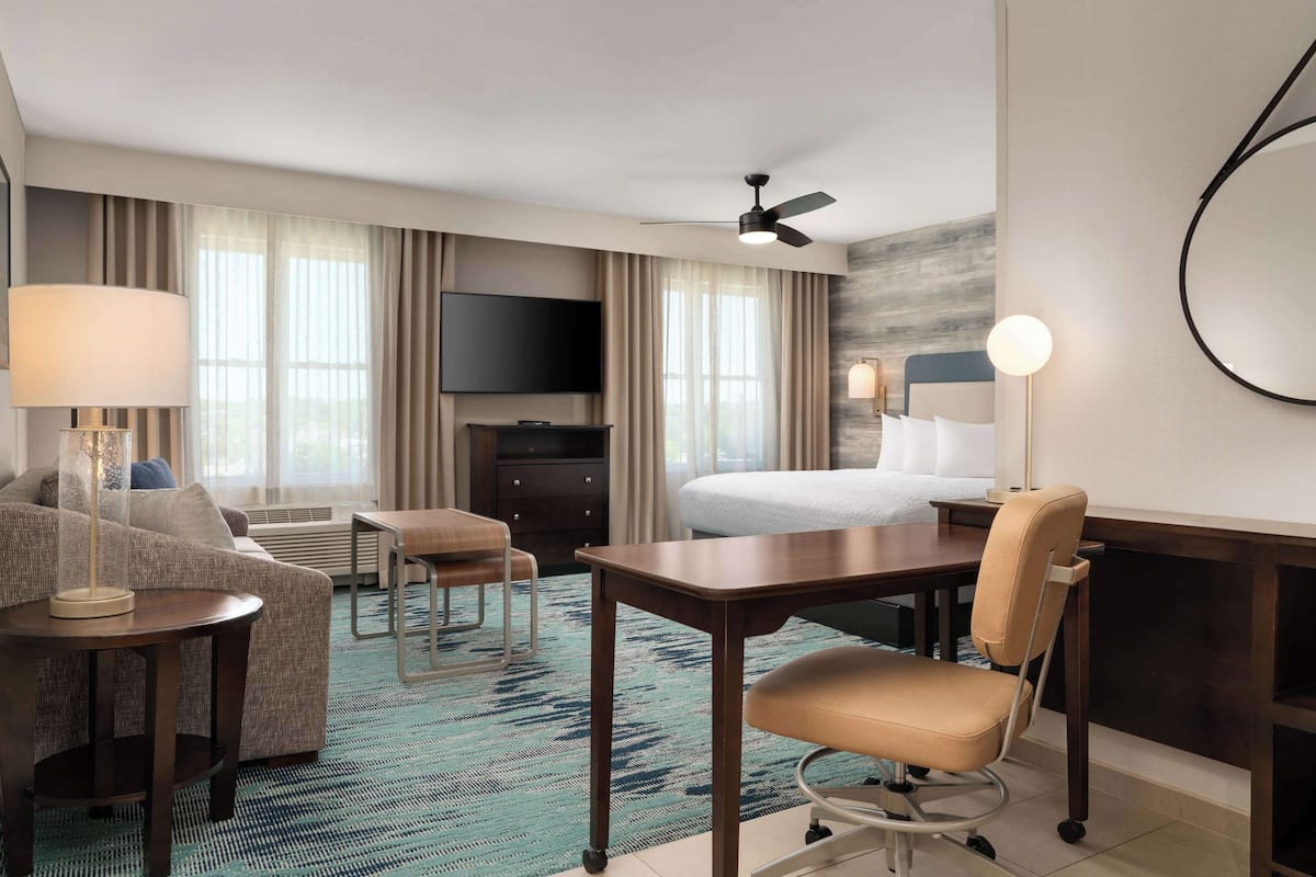 A hotel room with a bed, a desk, a chair, a TV, and a ceiling fan.