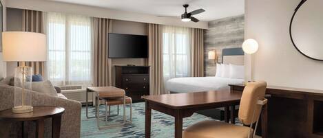 Ein Hotelzimmer mit Bett, Schreibtisch, Sessel, Fernseher und Deckenventilator.