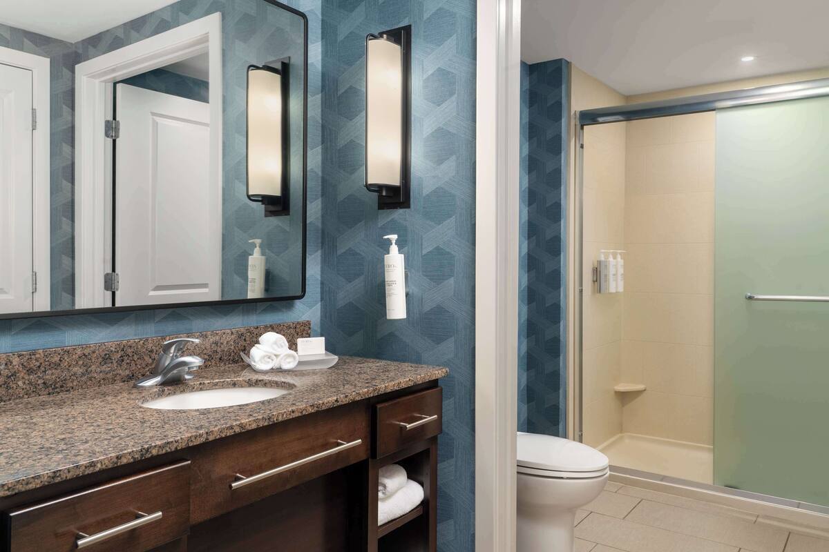 A bathroom with a granite countertop sink, a large mirror, and a glass-enclosed shower.