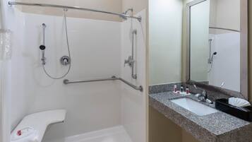 Un baño con ducha, barra de apoyo, inodoro, lavabo y espejo.