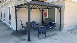 An outdoor seating area with a covered patio, tables, and chairs. - Baymont by Wyndham Victoria (Victoria)