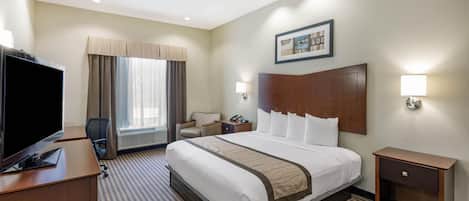 Habitación de hotel con cama, escritorio con televisor, silla, mesita de noche, lámpara y un cuadro en la pared.
