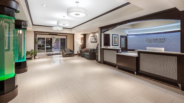 A modern reception area with a reception desk, a green-lit aquarium, and a seating area with a sofa and armchairs. - Baymont by Wyndham Victoria (Victoria)