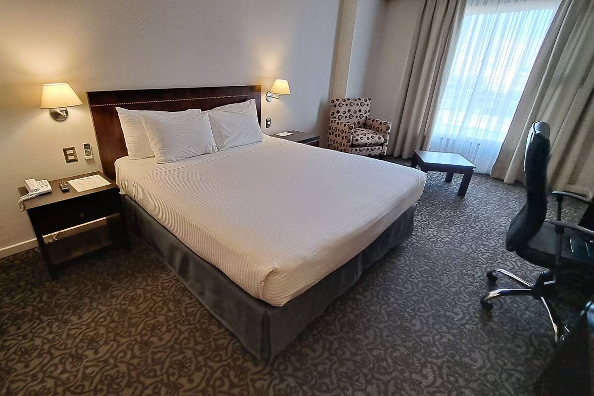 A hotel room with a large bed, two bedside tables with lamps, a chair, and a small table.