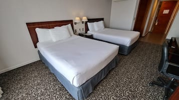 Une chambre d’hôtel avec deux lits, une moquette à motifs et un bureau avec une chaise.