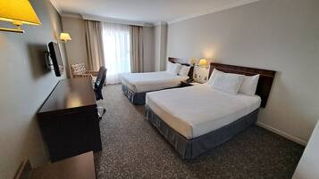 Una habitación de hotel con dos camas, un escritorio, una silla y un ventanal con cortinas.