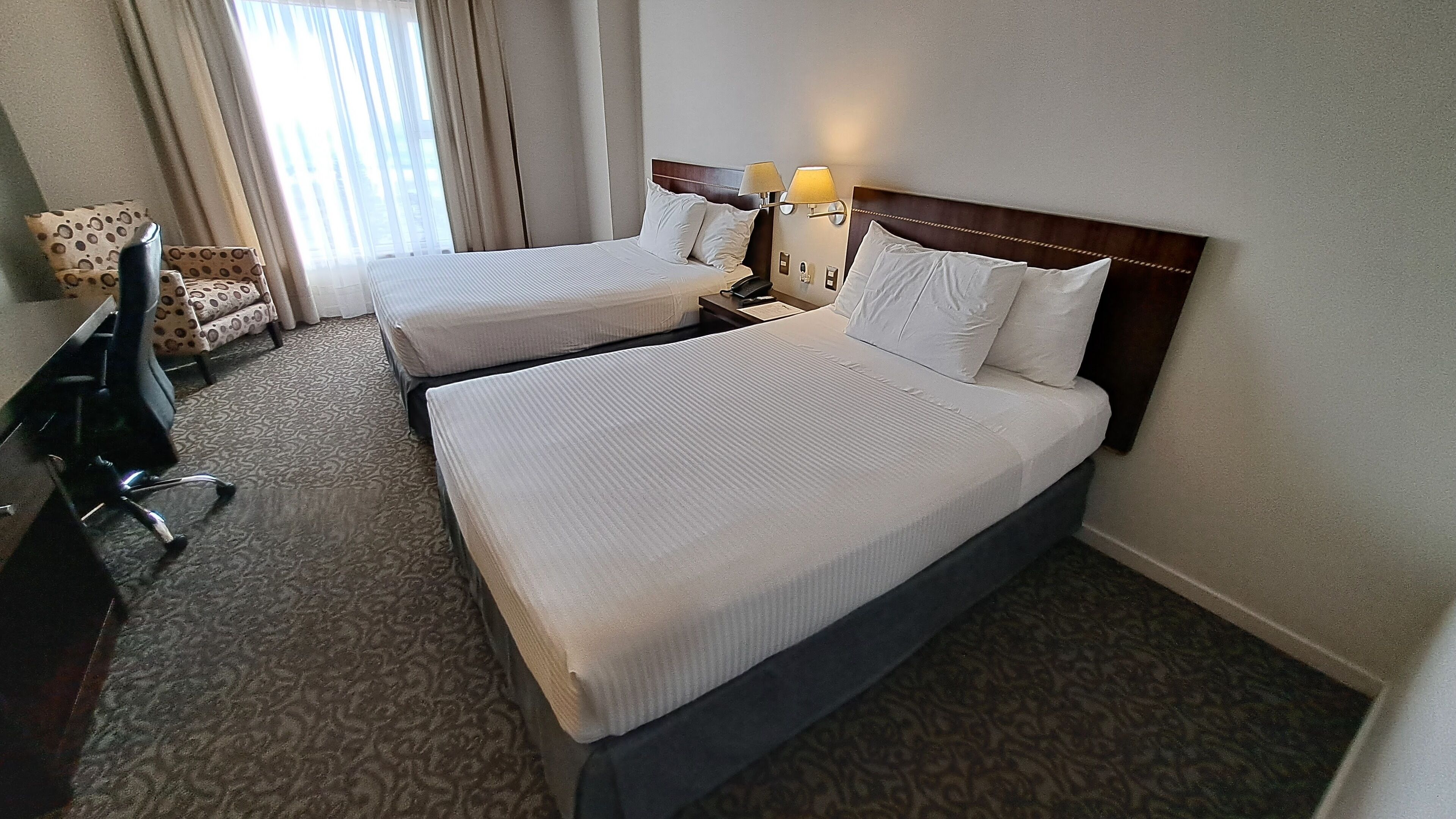 Una habitación de hotel con dos camas, un escritorio, una silla y una ventana con cortinas.