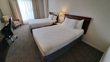 Una habitación de hotel con dos camas, un escritorio, una silla y una ventana con cortinas.