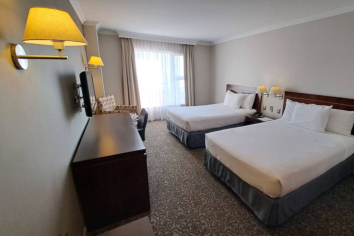 A hotel room with two beds, a desk, a chair, and a window with curtains.