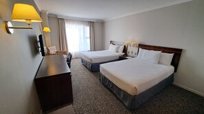 Una habitación de hotel con dos camas, un escritorio, una silla y un ventanal con cortinas.