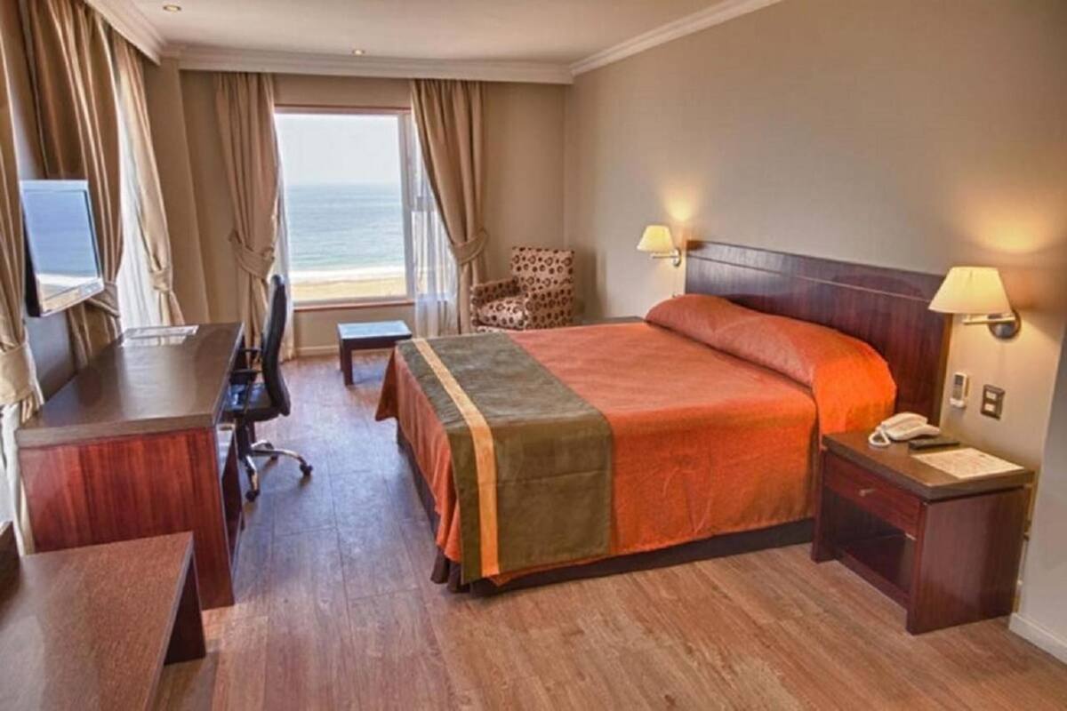 A hotel room with a bed, desk, chair, and a view of the ocean.