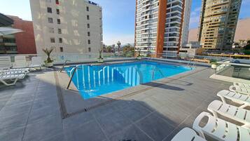 Une piscine sur le toit, avec une eau d’un bleu cristallin, entourée de chaises longues blanches et avec un bâtiment moderne en arrière-plan.