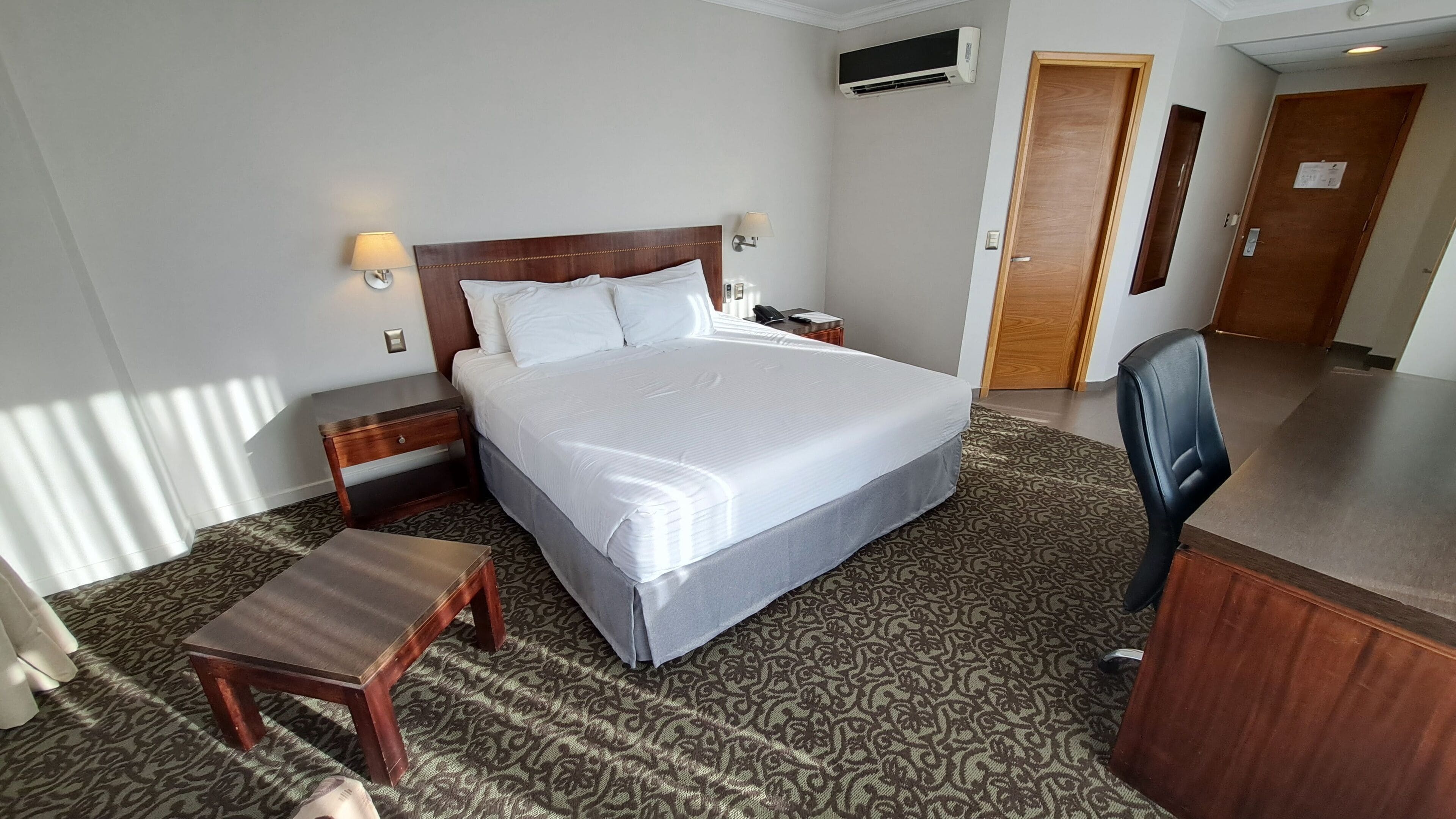 Una habitación de hotel con una cama grande, mesitas de noche, un escritorio, una silla y una alfombra estampada.