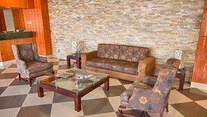 Un vestíbulo con mostrador de recepción, un sofá estampado, dos sillones y una mesa de centro de vidrio.