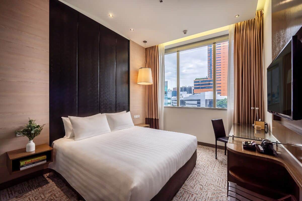 Ein Hotelzimmer mit einem großen Bett, einem Schreibtisch mit Stuhl, einem Fernseher und einem Fenster mit Vorhängen.