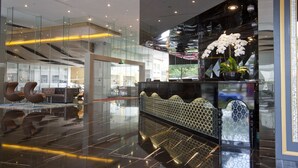 Een moderne lobby met glazen balustrades, een receptiebalie en eigentijds meubilair.