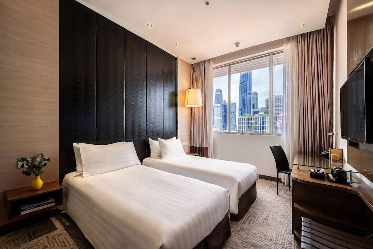Ein Hotelzimmer mit zwei Betten, einem Schreibtisch, einem Stuhl, einem Fernseher und einem Fenster mit Blick auf die Stadt.